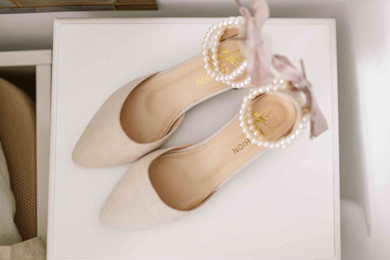 mobile-01 Top view of elegant bridal shoes with pearl and ribbon decor on a white surface, perfect for wedding fashion.