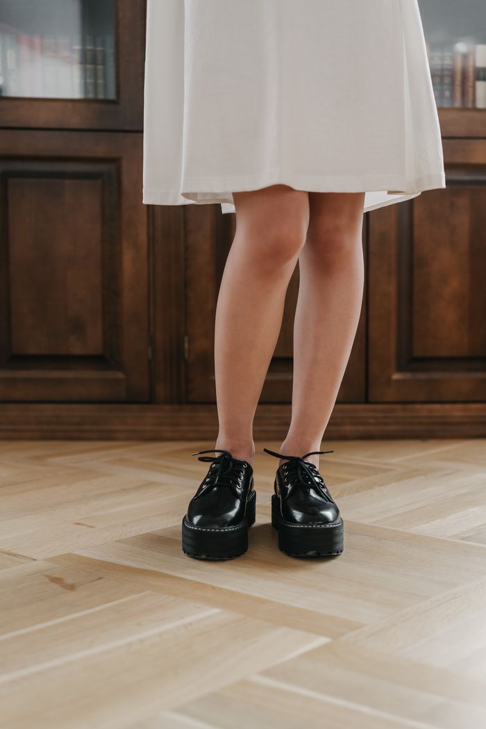creative-03 Elegant black shoes paired with a white dress, captured indoors on a wooden floor.